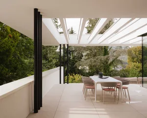 A well-lit outdoor patio with a white dining table surrounded by red chairs, set in a garden with a view of the mountains in the background