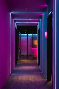 A modern hallway with pink carpet and glass walls, lit by purple lighting, creating a striking contrast and unique atmosphere