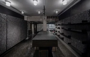 Modern kitchen with a dark countertop, a large window, and a dining table, featuring a sink and refrigerator, with dim lighting creating a cozy atmosphere