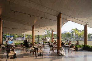 A large open space with a high ceiling, featuring various furniture, people, and natural light from windows, with a modern and stylish atmosphere