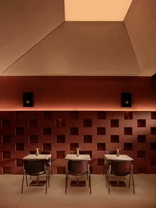 Cozy modern dining space with brown tables, black chairs, and a red brick pattern on the walls, lit by dim lighting