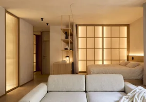 Cozy bedroom with a bed, couch, and bookshelf, set against a white wall and wooden floor, with dim lighting