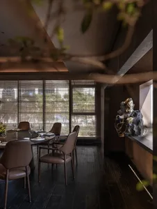 Dining room with a large window, modern dining table, chairs, wine glasses, potted plant, and vase, lit by natural light