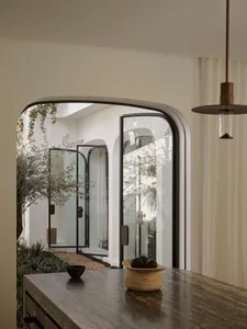 A well-lit modern dining room with a wooden table, chairs, and a potted plant, surrounded by a large window and a door