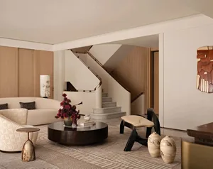 Furnished living room with a staircase, couch, chair, coffee table, and decorative vases, set in a well-lit and inviting space