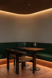 A modern restaurant dining area with a wooden floor, a dining table, chairs, and wine glasses, illuminated by a light source, creating a warm and inviting atmosphere