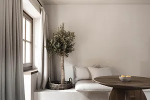 Comfortable living space with a white couch, dining table, and potted plant, well-lit through a window with a curtain