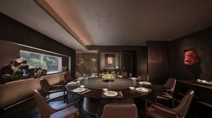 A dimly lit dining room with a round table set for a meal, surrounded by black chairs in a brown room