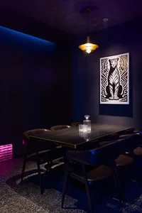 Dark dining space with a purple hue, featuring a leather dining table and chairs, and a tiger print on the wall