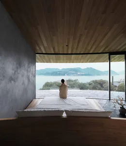 Serene bedroom with a large window offering an ocean view, a wooden headboard, and a white bed sheet in a well-lit space