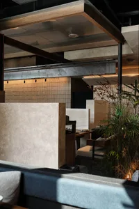 A modern restaurant space with a wooden floor, stone wall, and comfortable seating areas with dining tables and chairs, well-lit with natural light and a potted plant