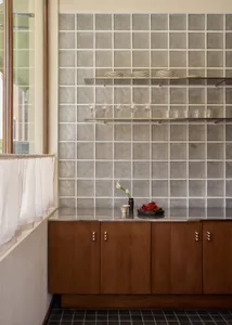 Modern kitchen with a wooden cabinet, tile backsplash, and natural light from a window, featuring wine glasses and a bowl on the countertop