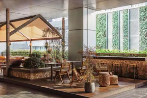 A dining area with a wooden table and chairs surrounded by potted plants, under a metal umbrella, in a restaurant or cafe setting
