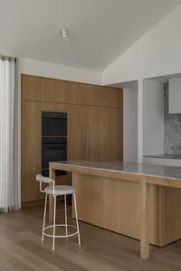 Modern kitchen with wooden cabinets, marble countertop, black oven, sink, refrigerator, chair, and dining table