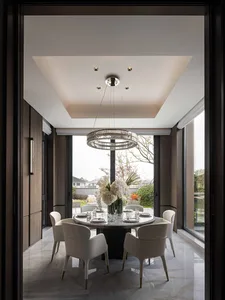 Dining room with a large wooden table and chairs, set with plates, wine glasses, and a vase of flowers, under a chandelier in a well-lit space