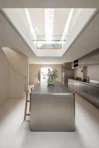 Modern kitchen with a stainless steel island, a dining table, and a refrigerator, featuring a minimalist and well-lit space with a vase with flowers on top of the island