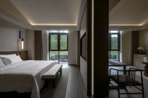 Cozy bedroom with a wooden floor, a bed, and a chair near a window, well-lit and inviting