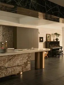 Photograph of a modern living room with a black and gold color scheme, featuring a piano, dining table, and counter, with a focus on luxury and sophistication