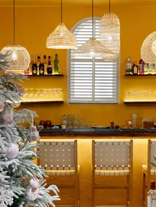 A well-stocked bar with a yellow wall, bottles, wine glasses, cups, and bowls, creating an inviting atmosphere for patrons
