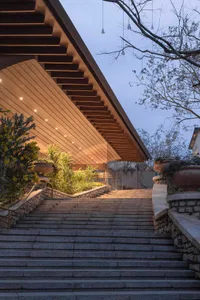 A modern building with a stone staircase leading up to a wooden door, set against a dimly lit background