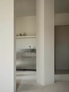 A clean and organized kitchen with a white color scheme, a stainless steel sink, and a refrigerator on the left side