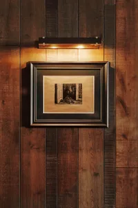 A dimly lit living room with a wooden floor, a couch in the center, and a chair to the right, creating a warm and intimate atmosphere