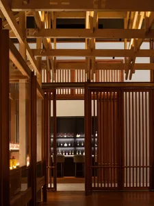 Dimly lit bar area with a wooden floor and black counter, featuring bottles and cups, creating a cozy atmosphere