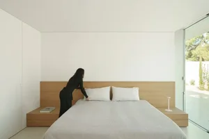 A cozy bedroom with a bed and nightstand, featuring a woman standing next to the bed, with a warm and inviting atmosphere