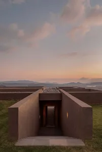 A modern building with a large open courtyard, concrete staircase, and wooden doorway, illuminated by natural light