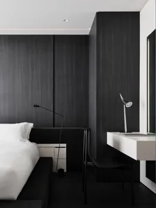 A dimly lit black and white bedroom with a bed, desk, and chair, creating a cozy and intimate atmosphere