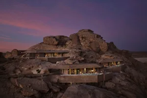 A modern villa situated on a hillside, surrounded by rocky landscape, with a swimming pool and outdoor furniture