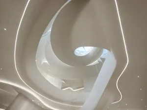 A minimalist museum with a spiral staircase made of concrete and glass railing, bathed in natural light from a window