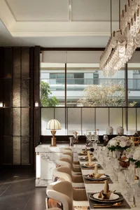 Dining room with a large window, a wooden dining table, and comfortable chairs, set for a meal, with a potted plant adding greenery, in a soft and warm lighting atmosphere