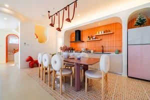 Warm and inviting kitchen with a dining table, wooden chairs, and a vase, surrounded by an orange color scheme and natural light