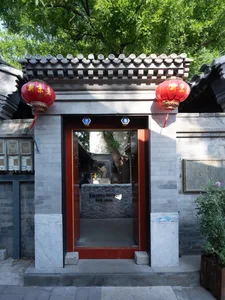 A photograph of a Chinese-style building with a red door and stone interior, set against a gray roof and surrounded by natural scenery, bathed in warm sunlight