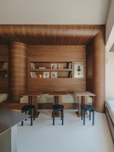 Warm and cozy living space with wooden walls and floors, a dining table, bookshelf, and couch, well-lit with natural light from windows
