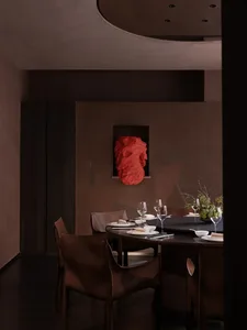 Dining room with a brown table and chairs, set with wine glasses, bowls, and cups, and a vase, in a dimly lit space with a cozy atmosphere