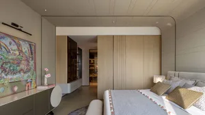 A modern bedroom with a wooden floor, a white bedspread, and a large window, with a bed positioned near the window and a dresser on the left side