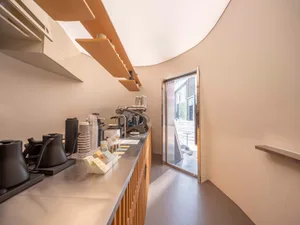 A modern kitchen with a wooden counter, coffee maker, and natural light from the open doorway