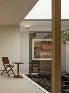 A modern living room with a glass wall, natural light, wooden furniture, and a potted plant, creating a bright and inviting atmosphere