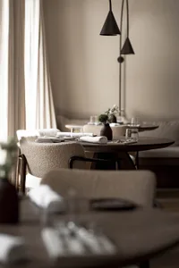 A modern restaurant dining area with white tablecloths, potted plants, and elegant decor, featuring a warm and inviting atmosphere