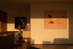 A well-lit living room with a couch, chair, and dining table, featuring a large painting on the wall
