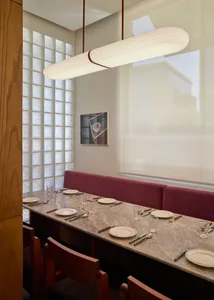 A modern dining room with a long wooden table and glass window, set with utensils and wine glasses, flooded with natural light