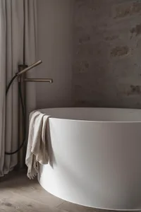 Dimly lit bathroom with a white bathtub under a window, a wool towel hanging on the side, and a cozy atmosphere
