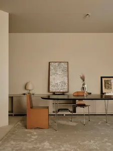 A well-lit dining area with a modern wooden table and chairs, a vase on the table, and natural light from a window