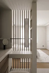 A modern bedroom with a bed, desk, and closet, decorated in white, with natural light entering through the window