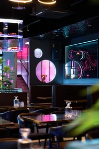 Modern restaurant with black and pink decor, featuring furniture, potted plants, and a stylish atmosphere