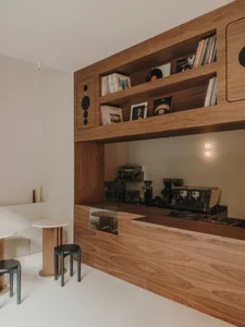 Cozy modern room with a wooden floor, counter, dining table, chairs, books, and a record player, lit by dim lighting