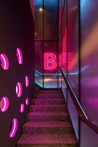 A staircase with purple steps and a pink wall, featuring a red neon sign and a vibrant color scheme