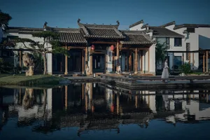 一張靜謐的黑白照片，描繪了一個典型的中國式建築物，屋頂上有個亭子，周圍有一個池塘和行道，庭院內有許多雕像佈置